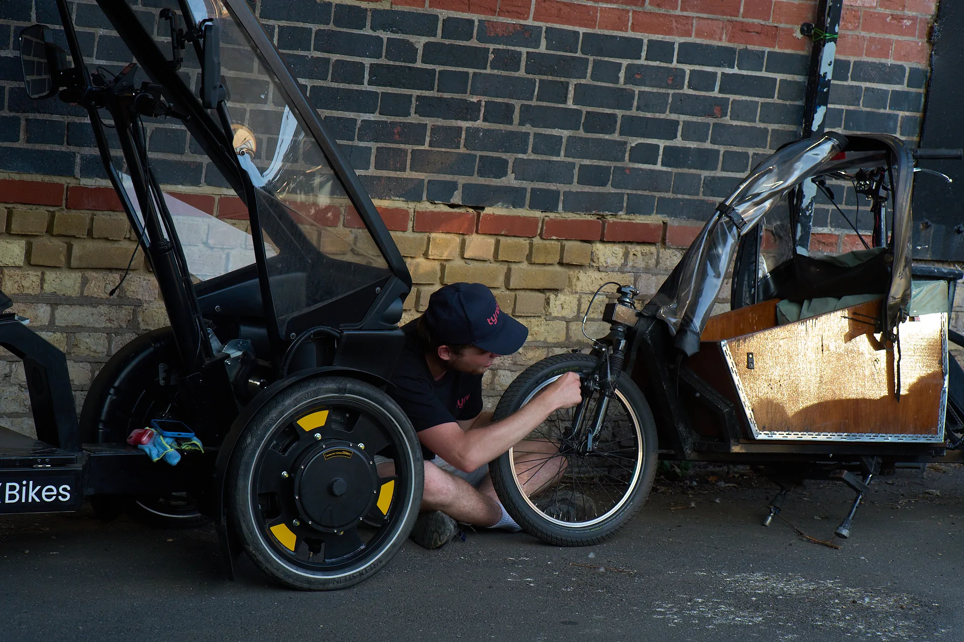 A Tyred mechanic servicing the wheel of a cargo bike on a London pavement.